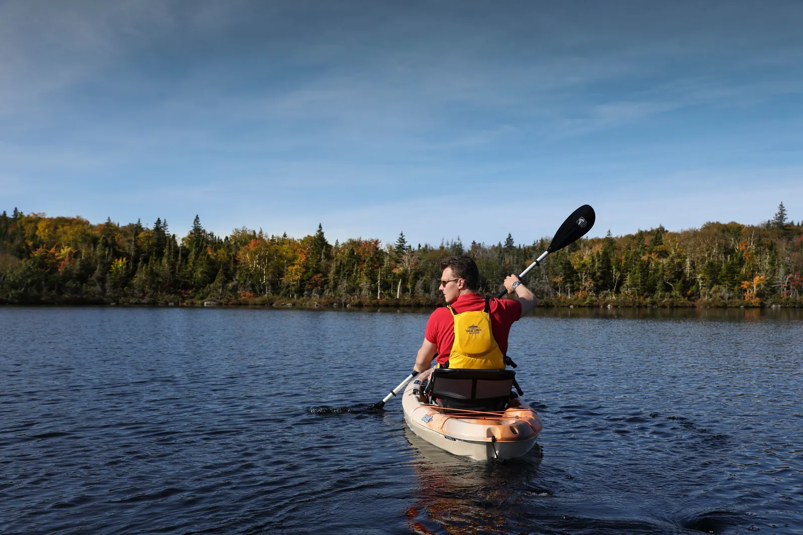 Kayaker paddling across a calm lake ringed by forest