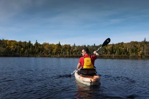 Kayaker paddling across a calm lake ringed by forest