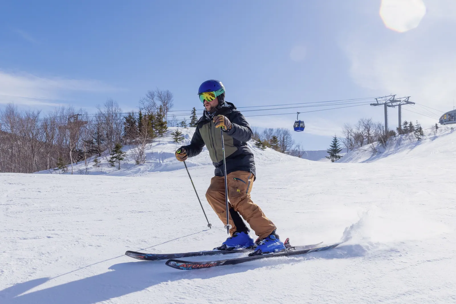 Skier on a groomed slope with Atlantic Gondola cabins and the lift line behind