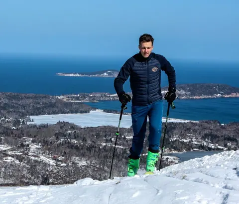 Skier with poles on the snowy summit, the Atlantic and islands behind