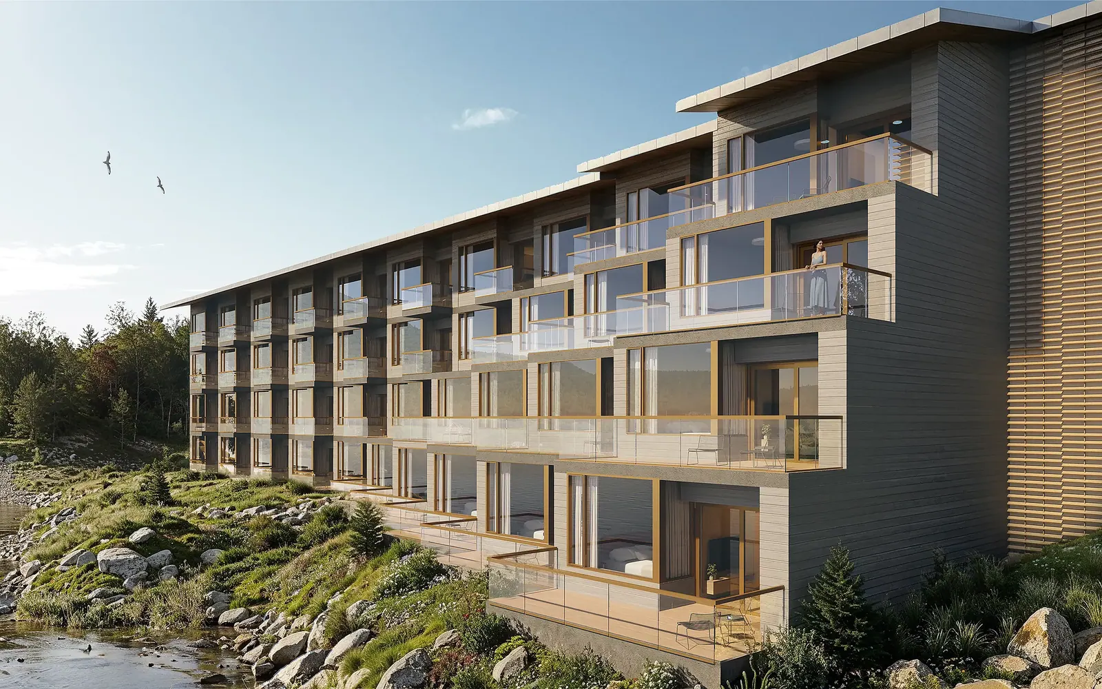 Close view of the Moose Hotel facade: stepped glass-fronted balconies with timber frames above a rocky, grassy shore