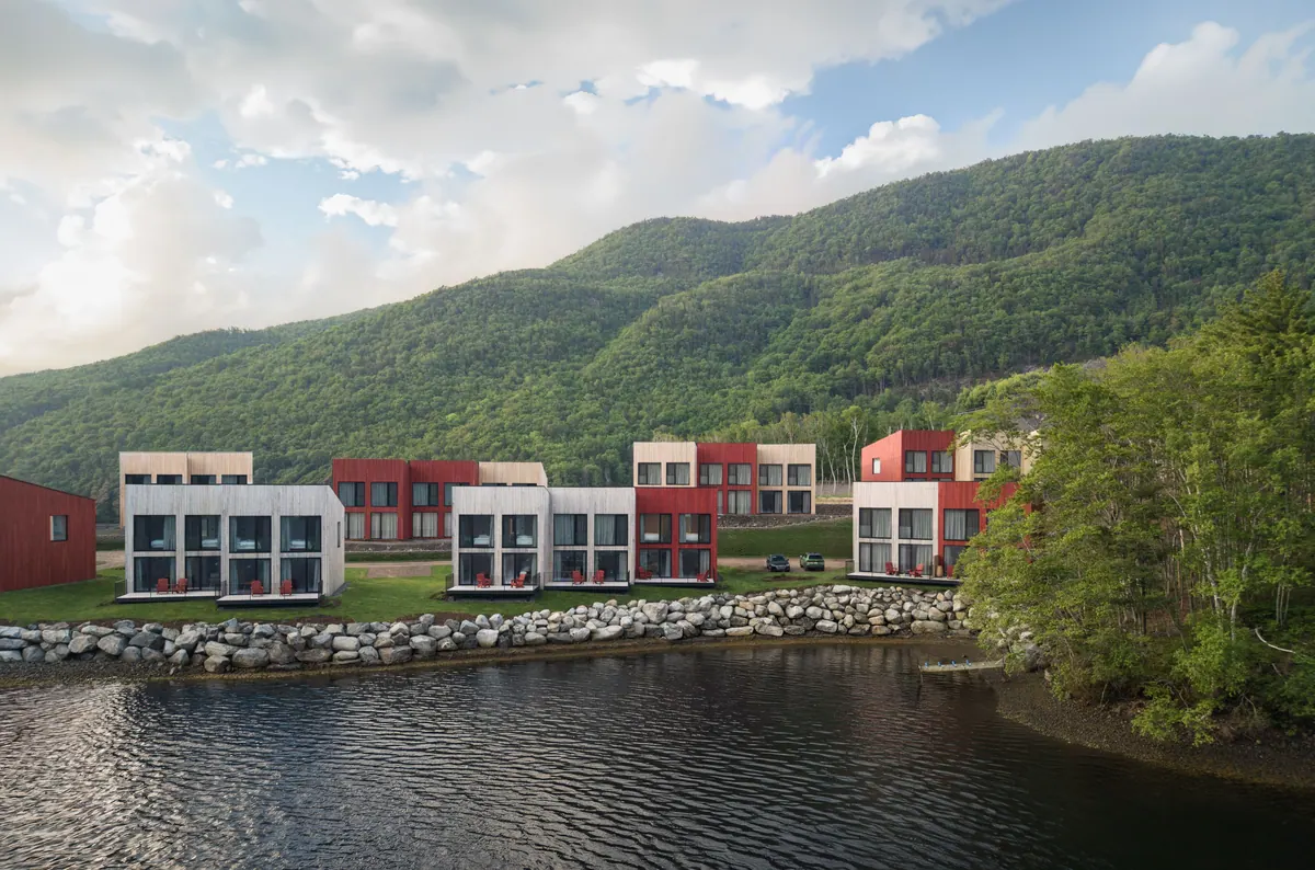 Cormorant Rock chalets on the shore below green forested hills in summer