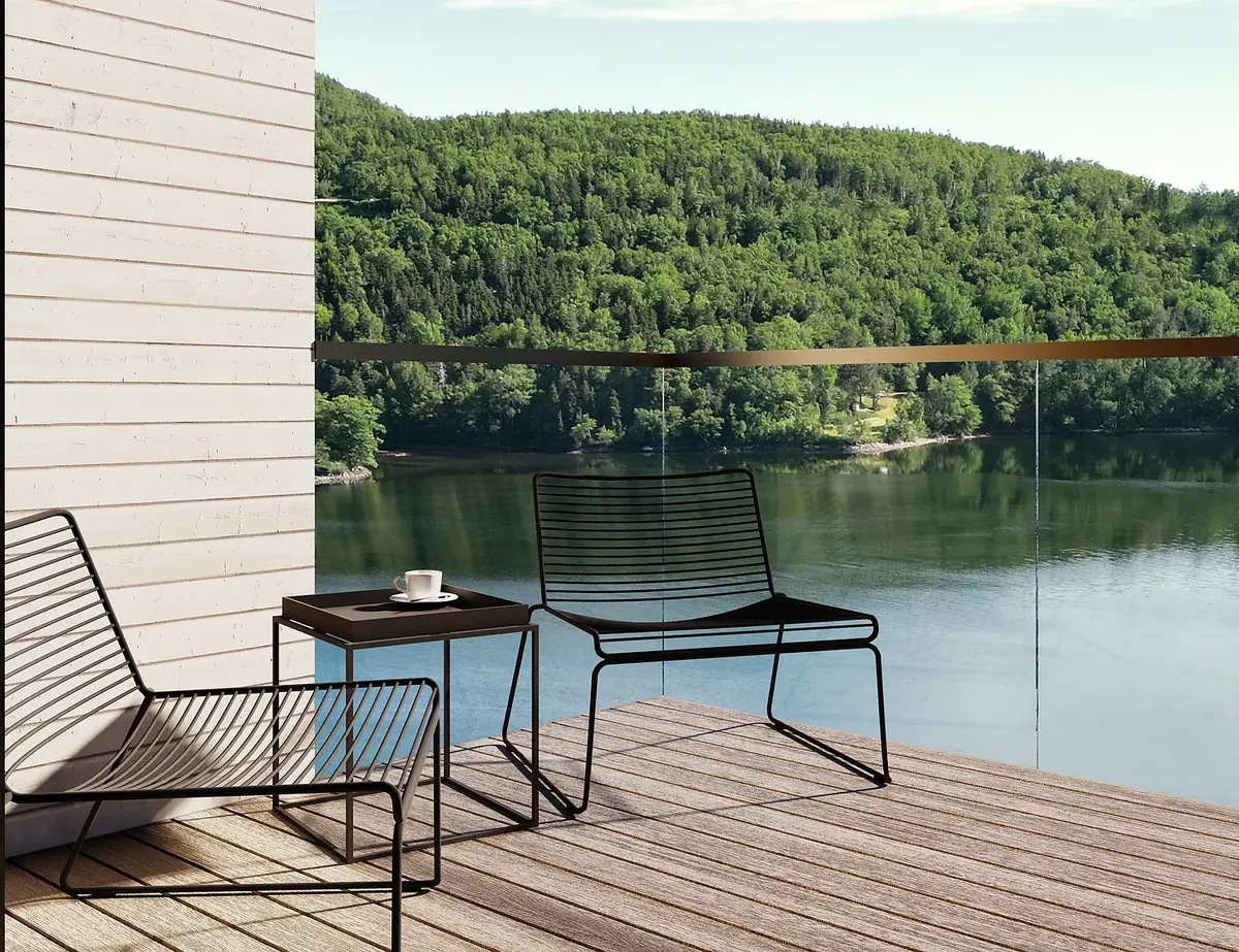 Two black wire chairs and a side table on a timber terrace overlooking a forested lake