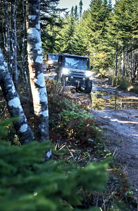 Off-road vehicle with headlights on a muddy forest trail