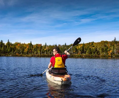 Kayaker paddling across a calm lake ringed by forest