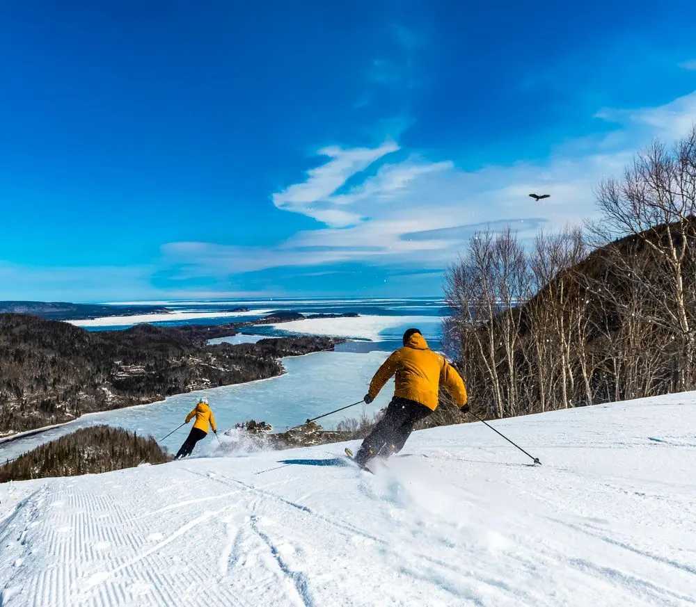 Two skiers carving down a groomed run above the frozen bay and the Atlantic