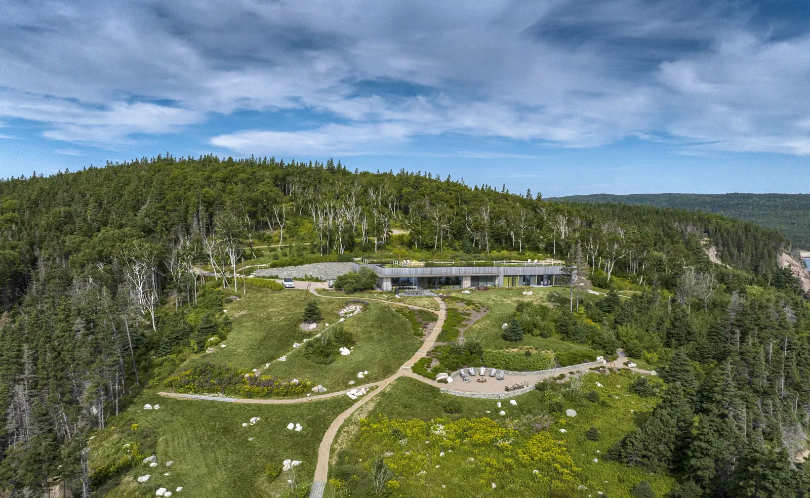 Aerial view of the Red Head Cliffs house set into a green clearing with winding paths, surrounded by forest
