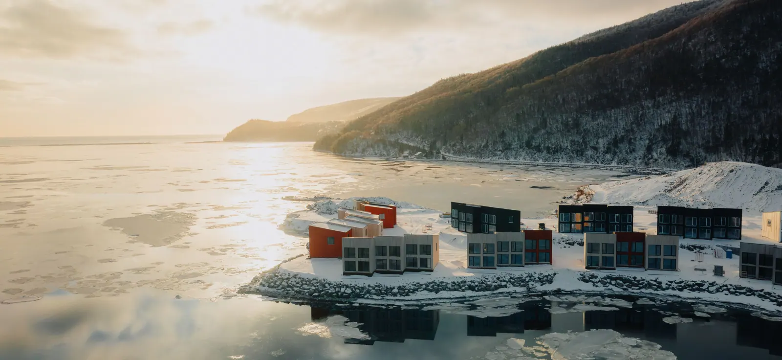 Cormorant Rock chalets on the rocky shore in winter, with Cape Smokey rising behind the bay