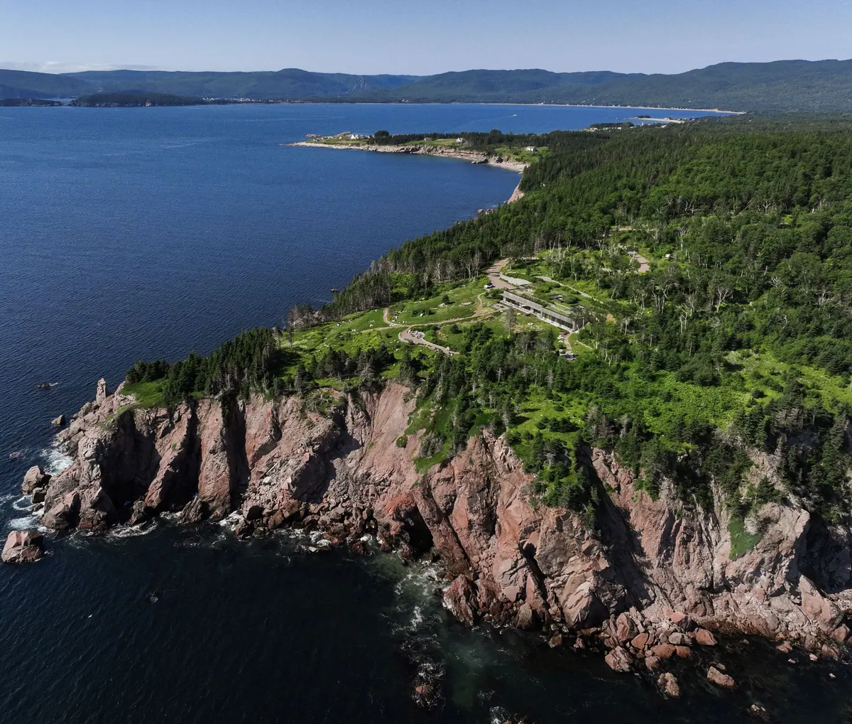 Aerial view of Red Head Cliffs: the low house among green meadows on top of red granite cliffs above the Atlantic bay