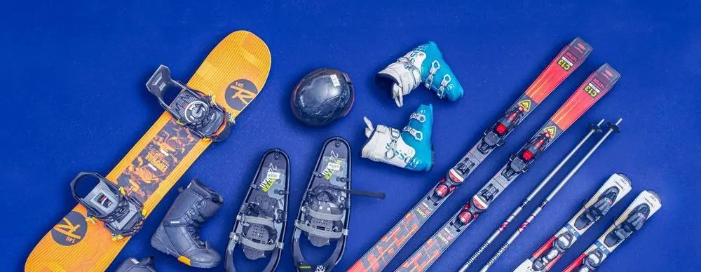 Snowboard, ski boots, snowshoes, helmet, poles and skis laid out on a blue background