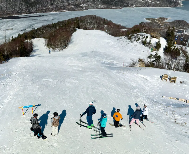 Aerial view of a ski lesson group gathered on a groomed slope above the frozen lake