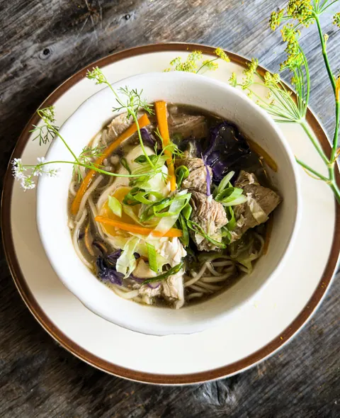 Bowl of chicken noodle soup with fresh herbs on a wooden table