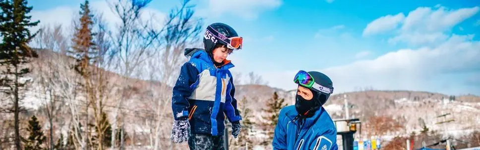 Young skier in a helmet and goggles with a Snow School instructor on a sunny slope