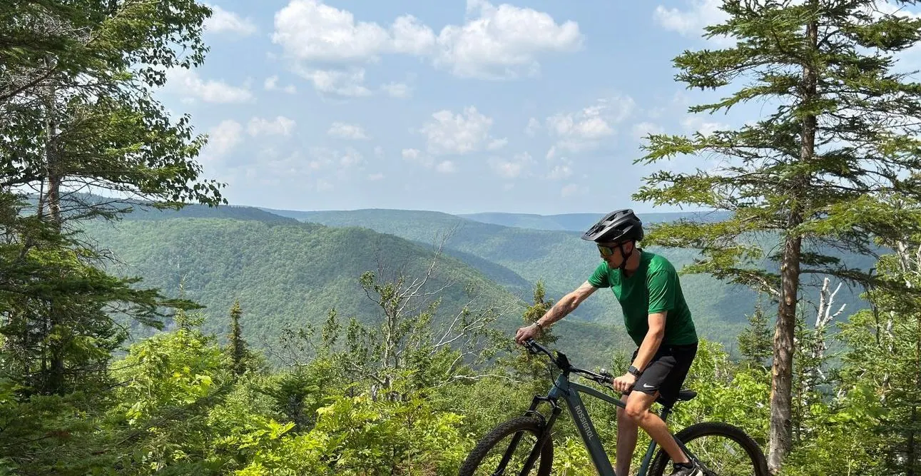 Rider on an e-bike on a summit trail above forested hills
