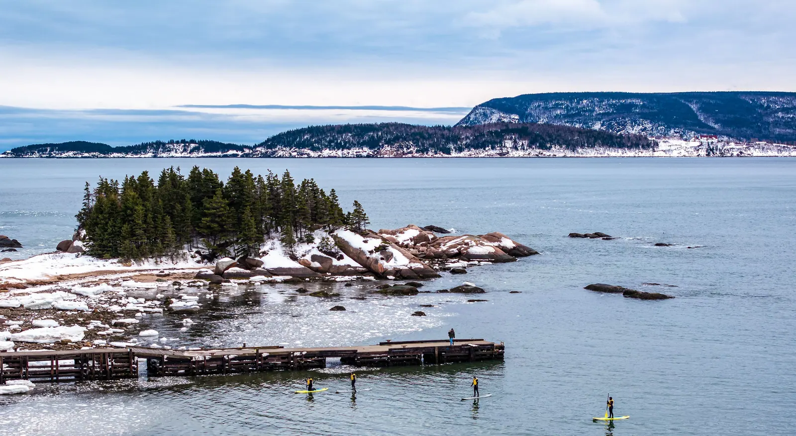 Snow-covered island with spruce trees and a wooden pier on the Atlantic, Cape Smokey on the horizon