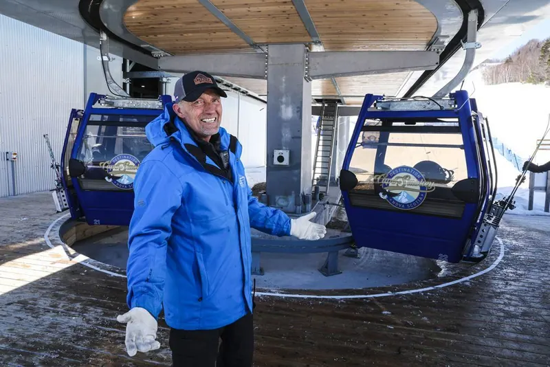Cape Smokey team member welcoming guests in the gondola station beside two gondola cabins