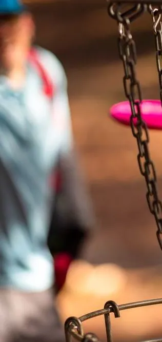 Player throwing a pink disc at a disc golf basket