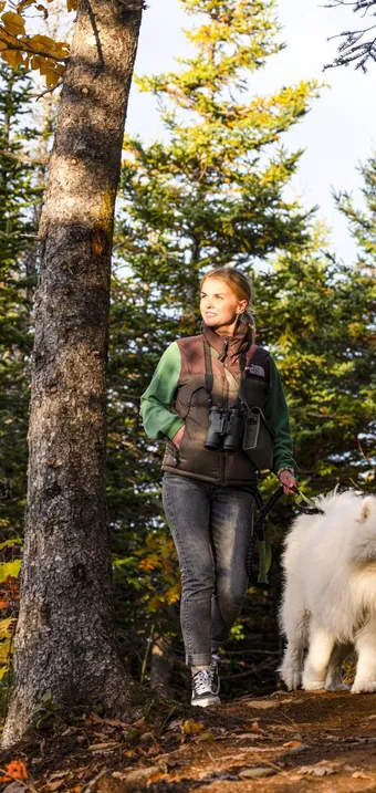 Hiker with binoculars and a white dog in the forest