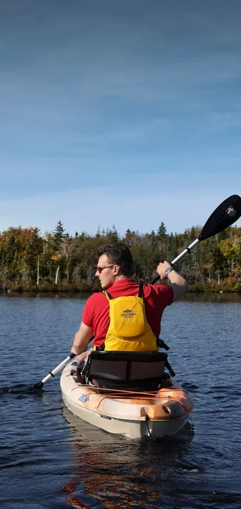 Kayaker paddling on a calm lake lined with early autumn forest