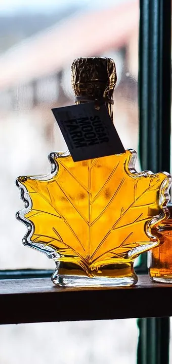 Maple syrup in a maple-leaf bottle and small jars on a sunny windowsill