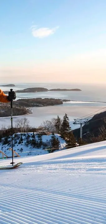 Ski tourer skinning up a groomed slope with the bay and gondola behind