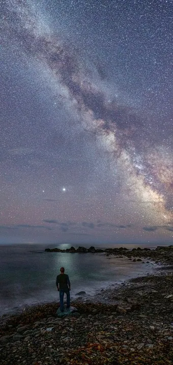 The Milky Way rising over the dark ocean and rocky shore