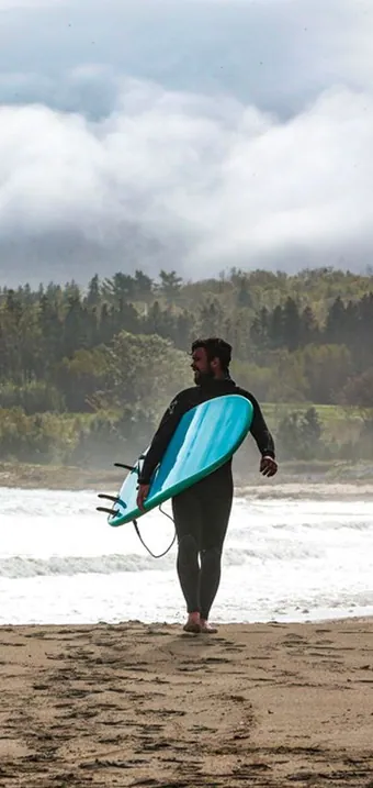 Surfer carrying a board along the beach out of the waves