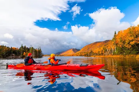 Two paddlers in a red kayak on a lake below autumn hills