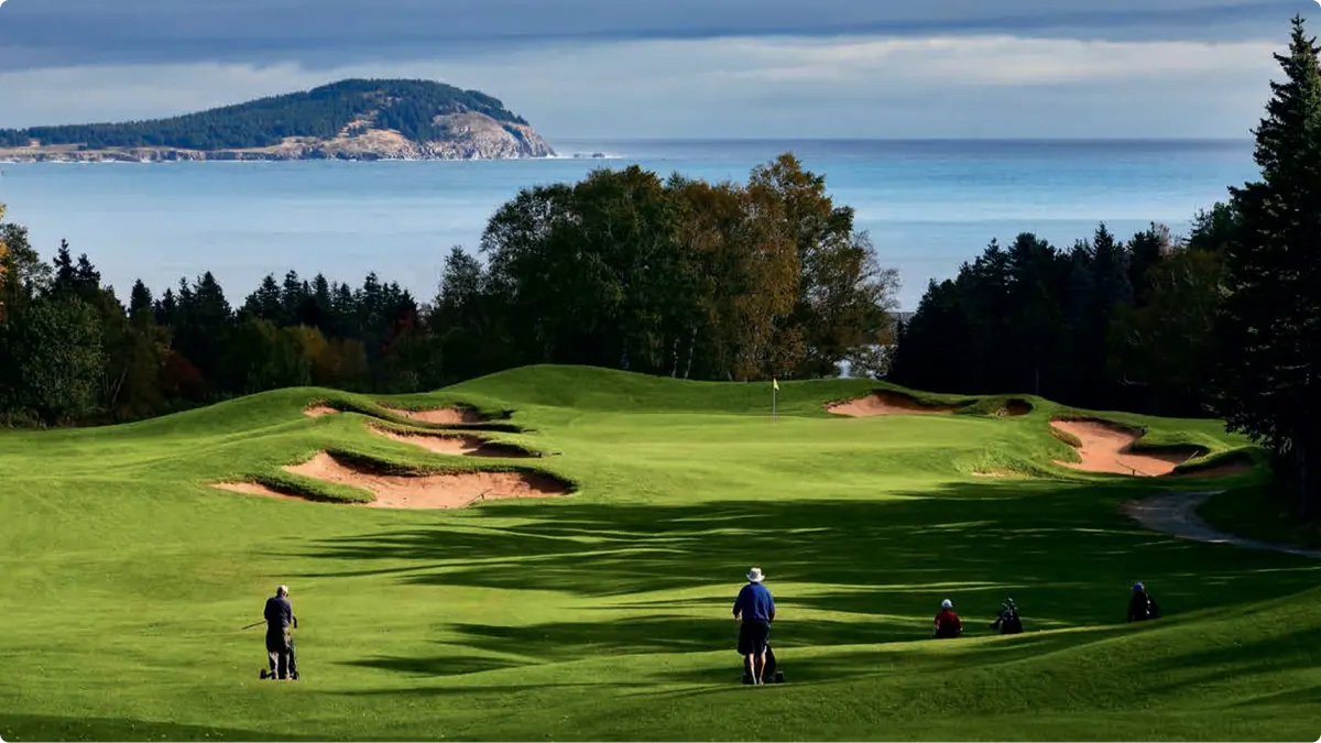 Golf green with sand bunkers and golfers, the ocean and an island beyond