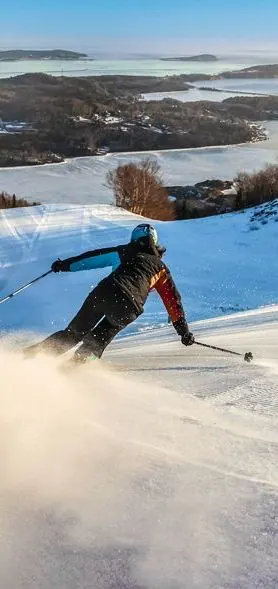 Skier carving a turn on a groomed run above the frozen bay