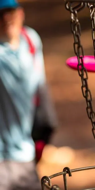 Disc golf basket chains with a player in the background