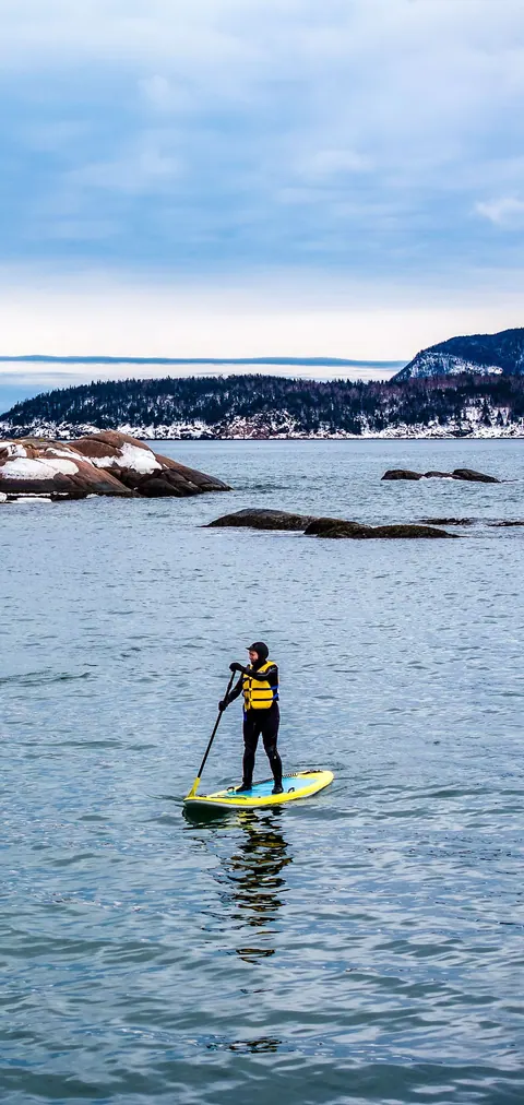 Paddle boarder on calm water near the rocky shore