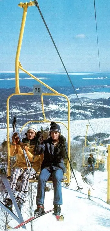 Vintage photo of two skiers riding a chairlift above the ocean
