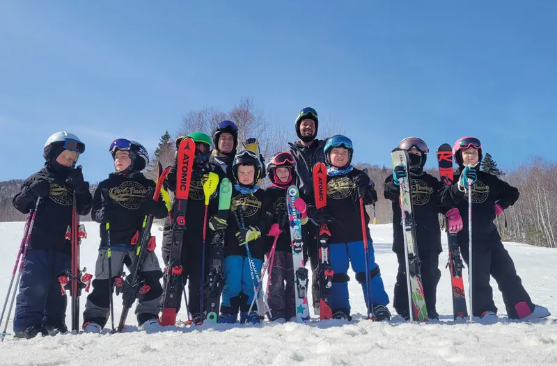 Snow School instructors and young skiers lined up with their skis at the top of the hill
