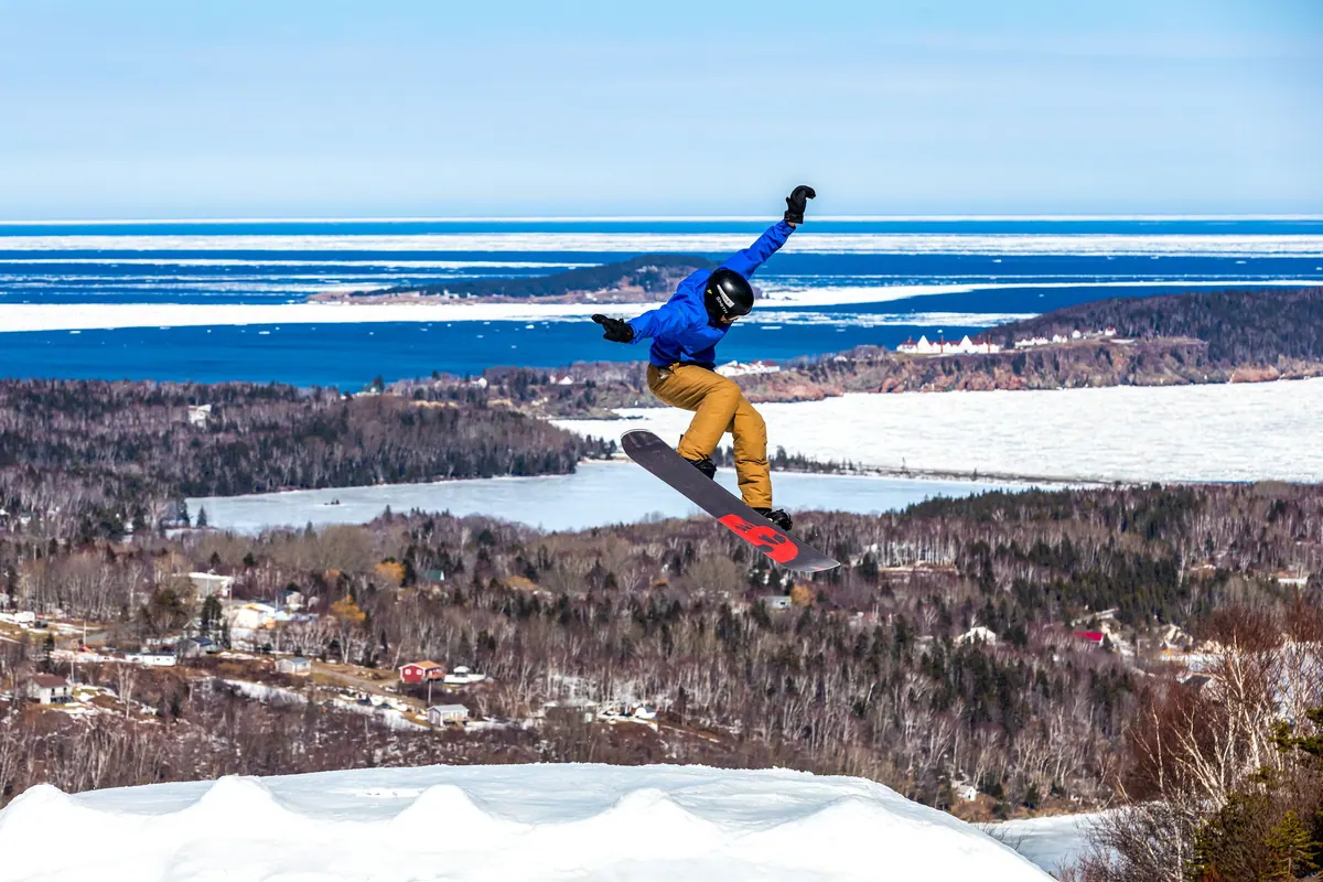 Snowboarder jumping above the slope with the ocean and village below