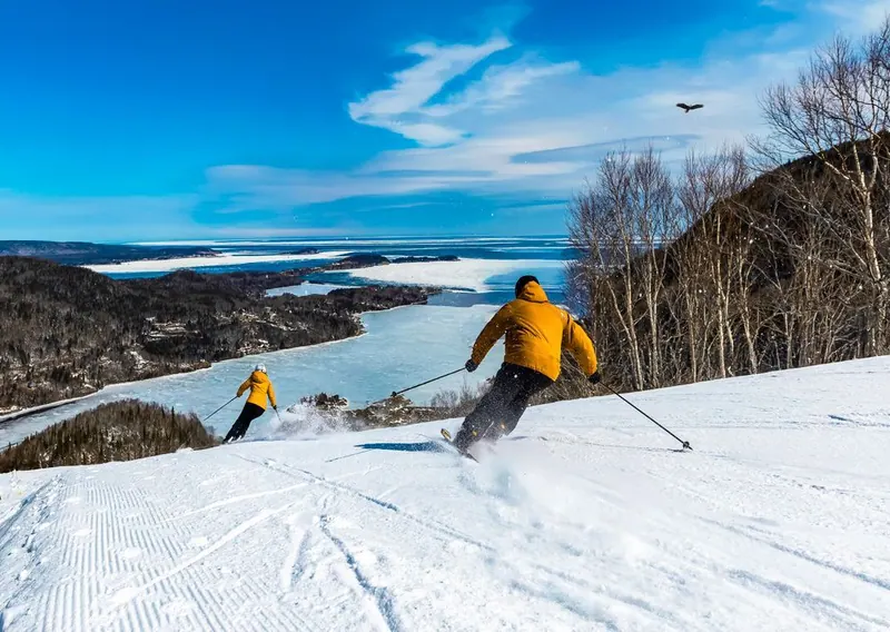 Skiers carving down a groomed run above the frozen bay