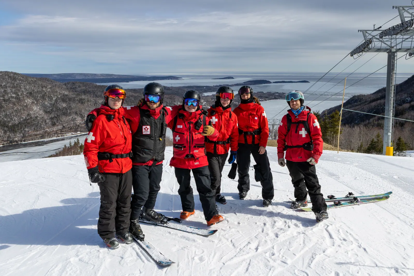 Cape Smokey Ski Patrol team in red jackets on the snowy summit above the bay