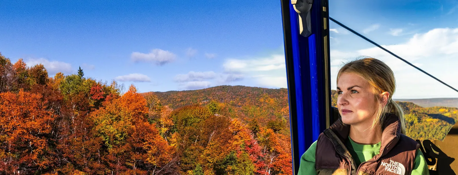 Visitor in a gondola cabin above bright red and orange autumn forest