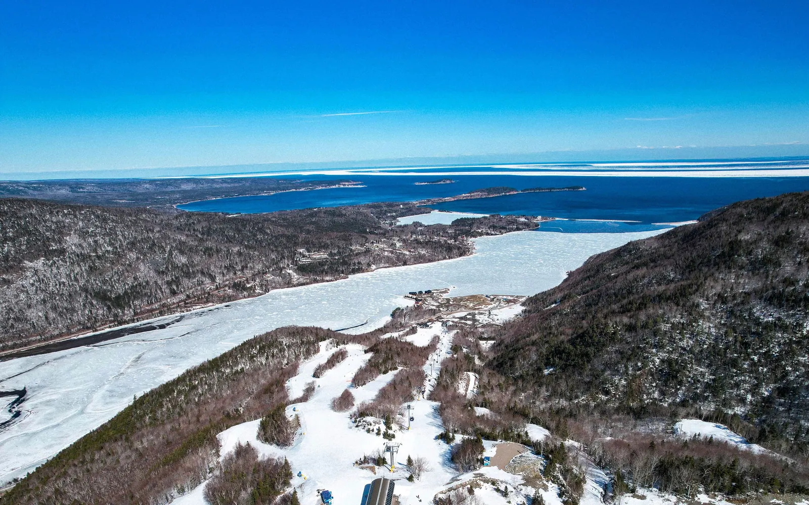 Aerial view of snowy ski runs and forest above the frozen river and the Atlantic coast