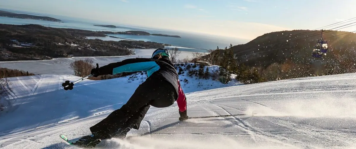 Skier leaning into a turn on a groomed run above the bay, gondola cabin in the distance