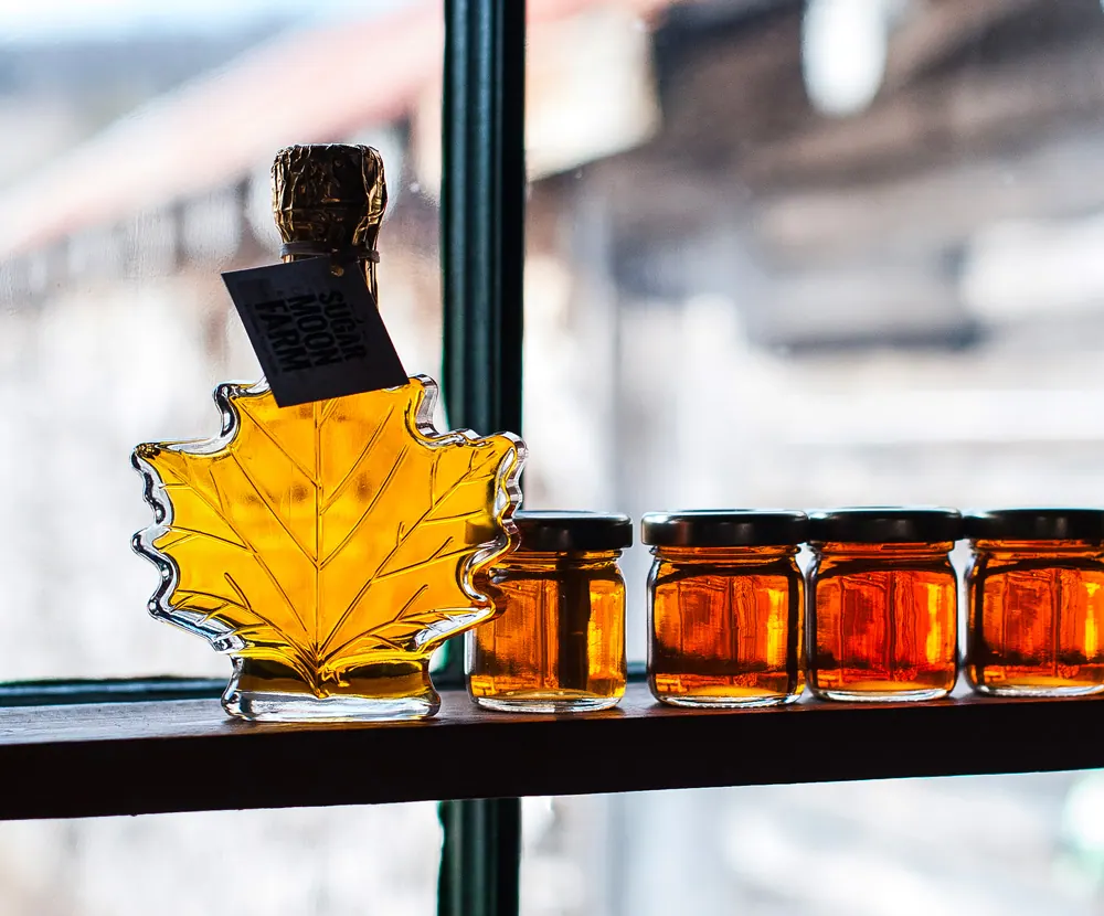 Maple syrup in a maple-leaf bottle and small jars on a sunny windowsill