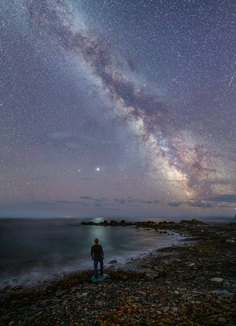 The Milky Way rising over the dark ocean and rocky shore