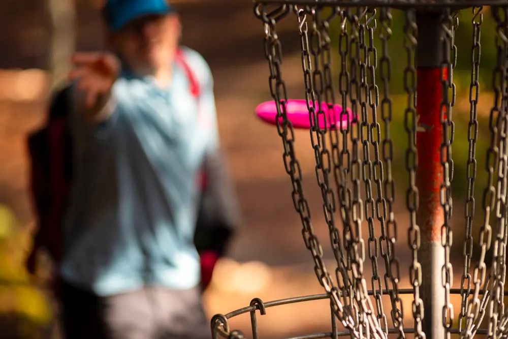 Player throwing a pink disc at a disc golf basket