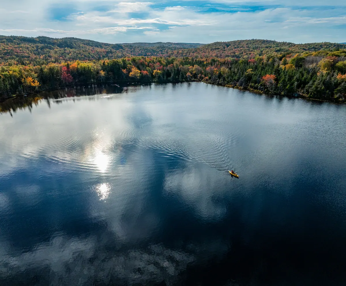 Aerial view of Hawley Lake reflecting the clouds, with a kayak on the water
