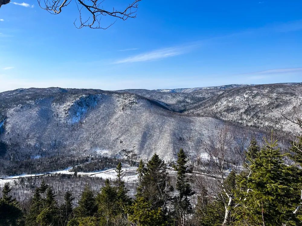 Snow-dusted highland valley under a blue sky, seen from the summit