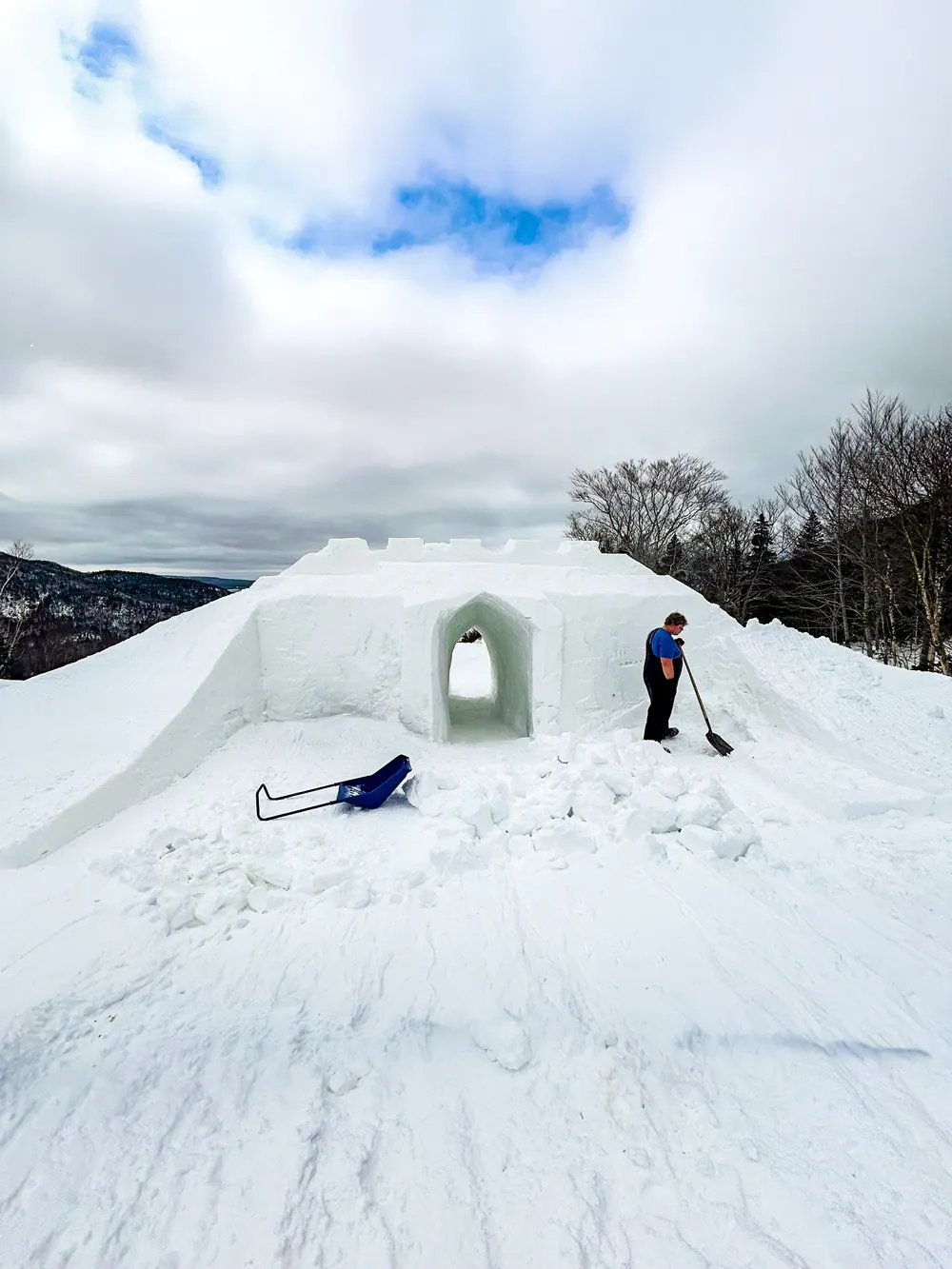 Snow castle with an arched doorway being shaped by a person with a shovel