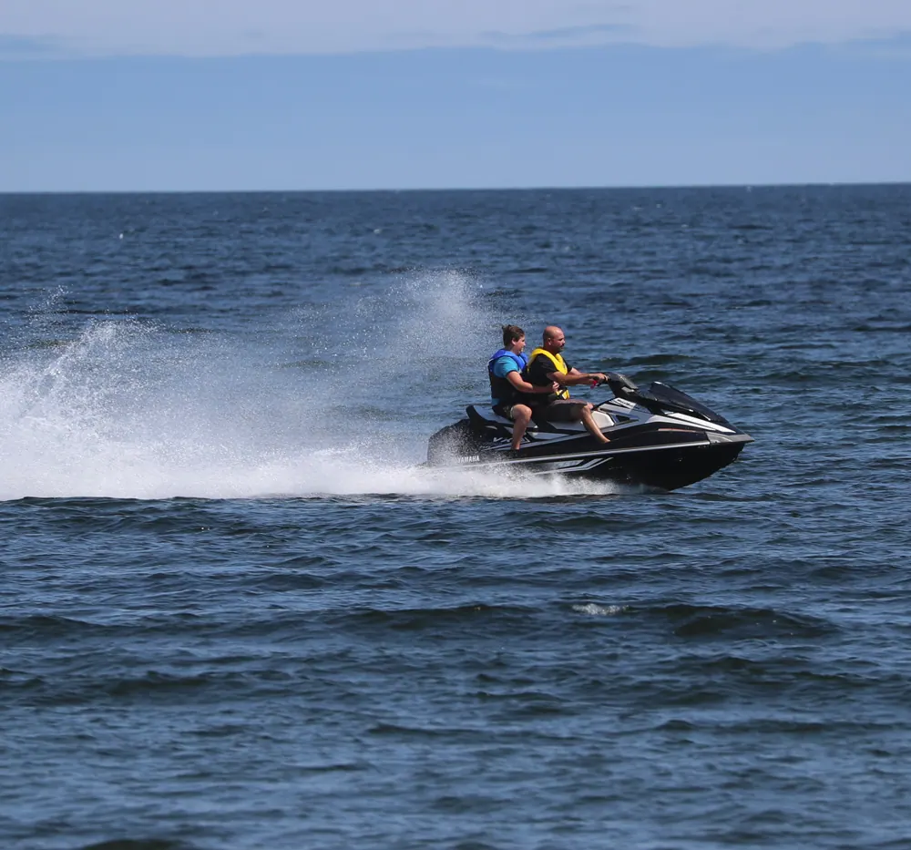 Two riders on a jet ski speeding across the ocean