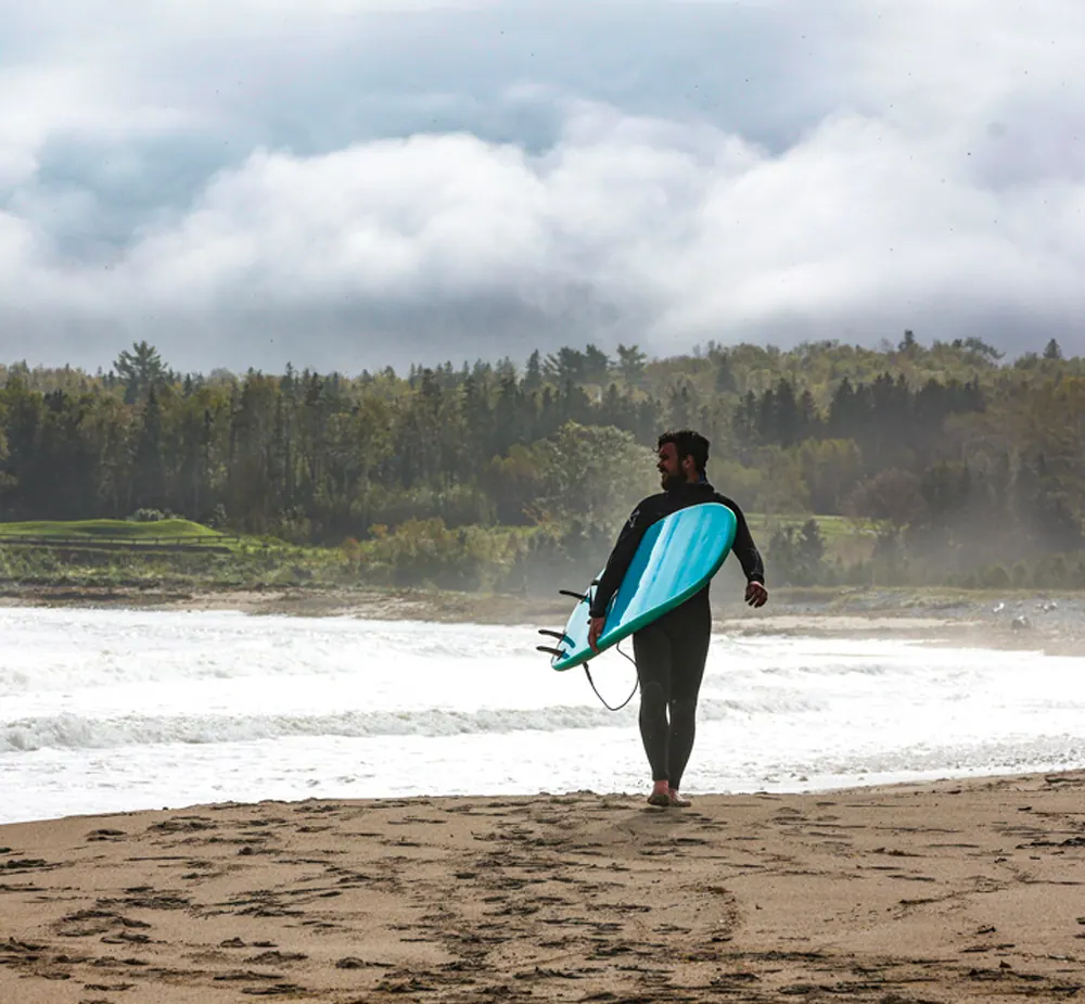 Surfer carrying a board along the beach out of the waves