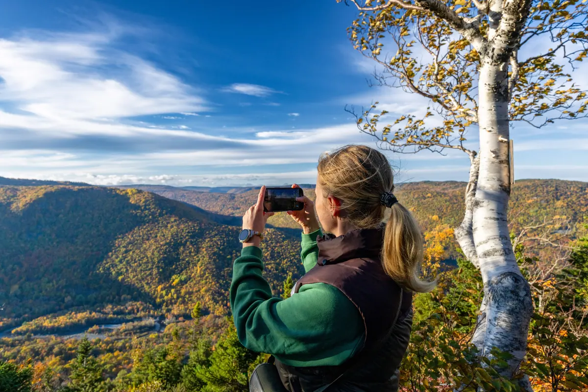 Hiker photographing the forested highlands valley from a lookout