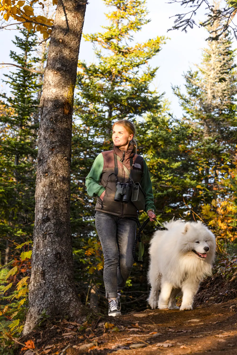 Hiker with binoculars and a white dog in the forest